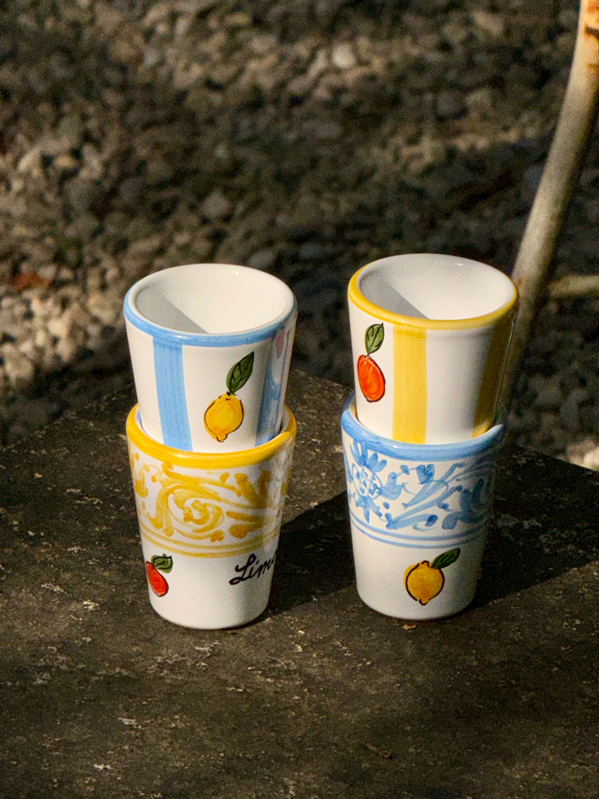Vier handbemalte Keramikbecher in blau-weiss gestreift mit Zitronendekor, weiss mit blauen Ornamenten und Zitronendekor, gelb-weiss gestreift mit Orangendekor und weiss mit gelben Ornamenten und Orangendekor