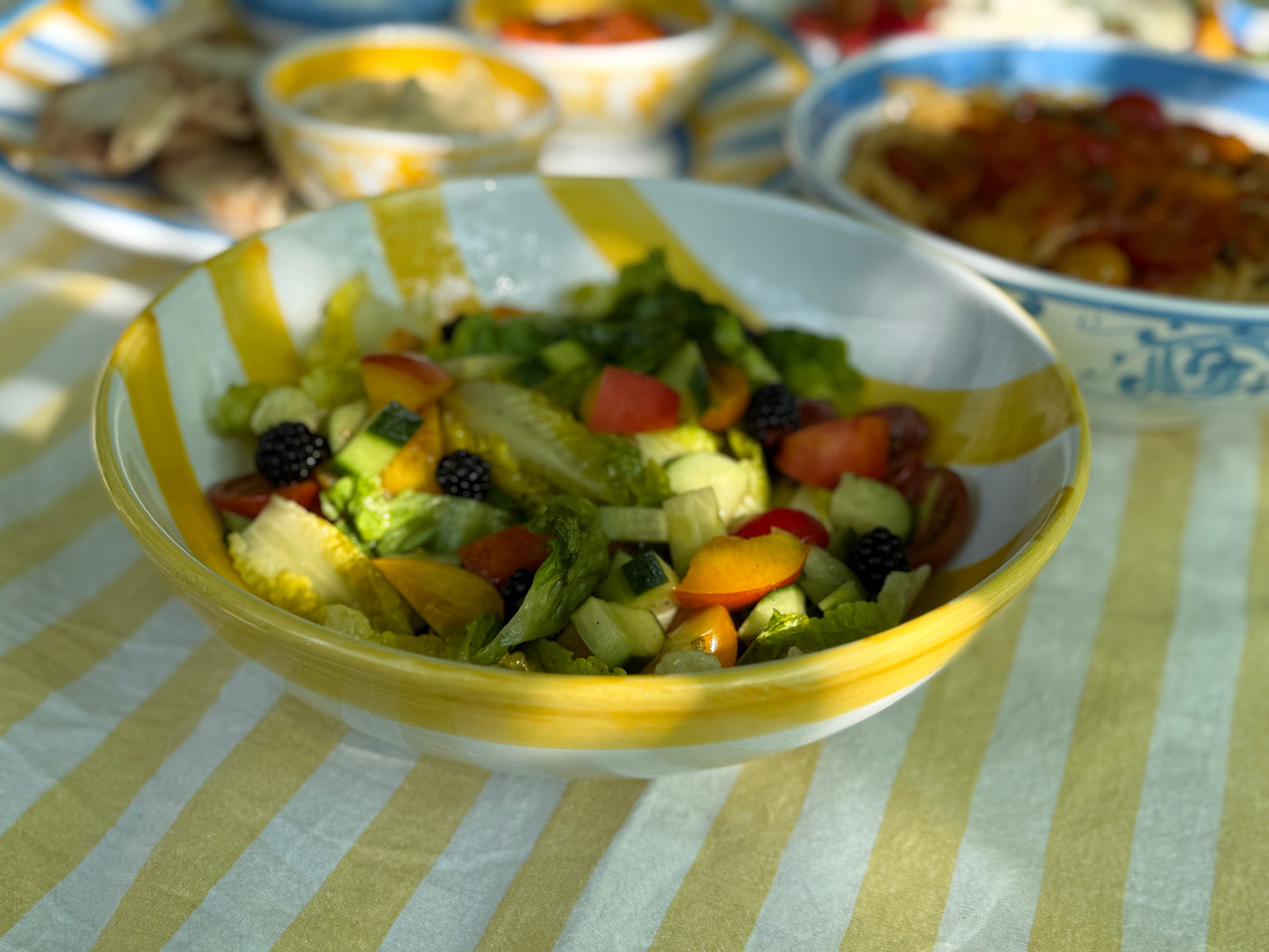 Sommerliche Tavolata mit buntem Salat in gelb-weiss gestreifter Salatschüssel