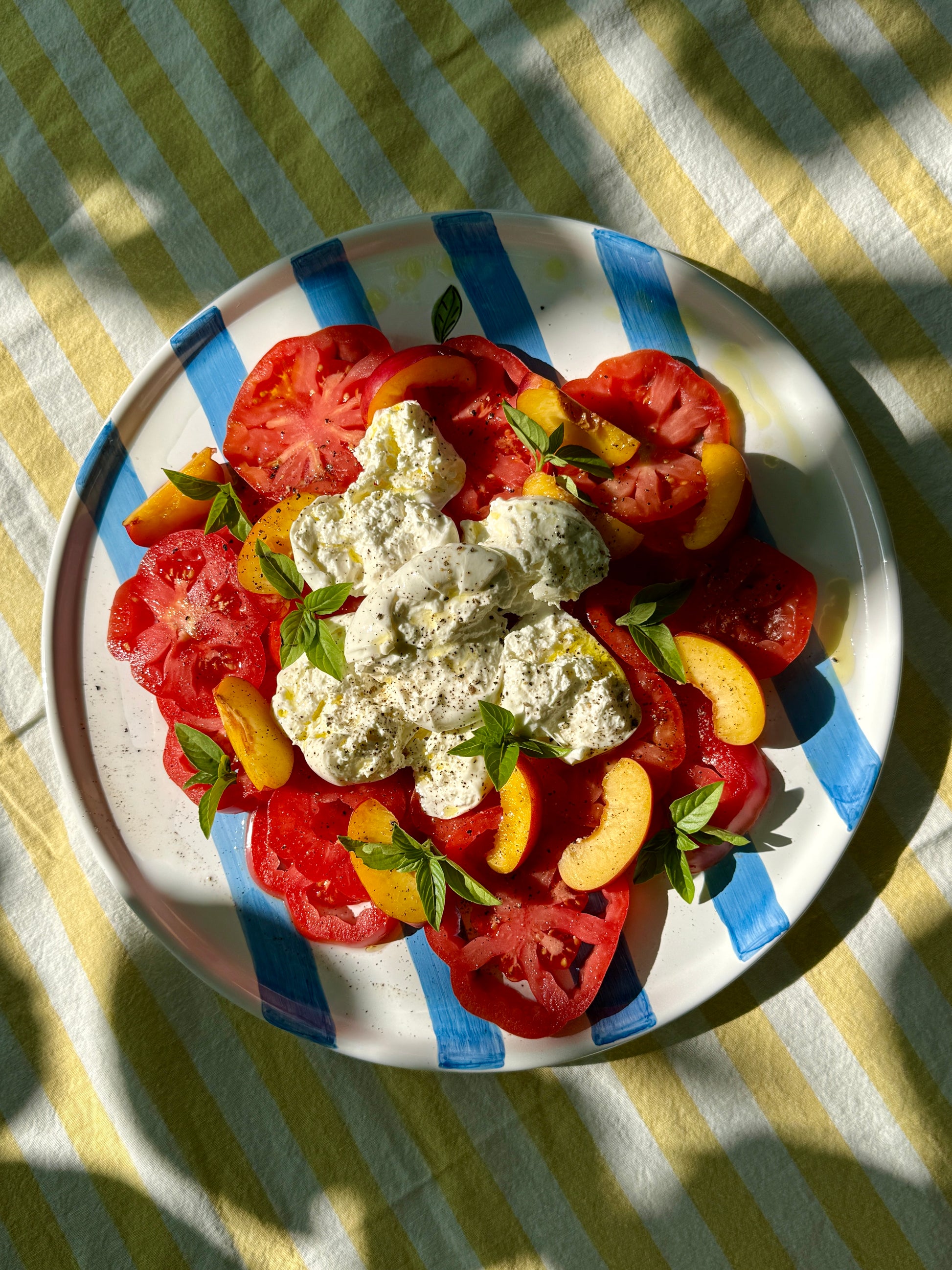 Handbemalte sizilianische Servierplatte aus Keramik, blau-weiss gestreift, mit sommerlichem Caprese Salat und Pfirsichen